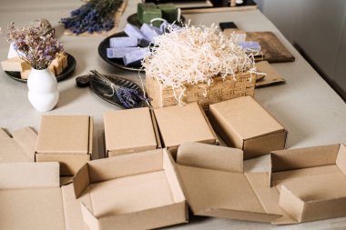 Temiz bir çalışma alanındaki el yapımı sabunların ve parçalanmış dolguların yanına yerleştirilmiş boş kraft kutuları. Ölçeklenebilir ambalaj, modüler kutu sistemi, ekommerce adaptasyon, kompakt ambalaj eğilimi. Yüksek kalite fotoğraf