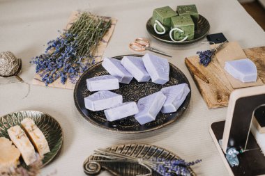Lavanta ve yeşil sabunlar kurumuş çiçeklerle ve kesme aletleriyle bir masaya dizilmiş. Aromaterapatik sabun, lavanta faydaları, fonksiyonel sağlık, bitkisel koku. Yüksek kalite fotoğraf