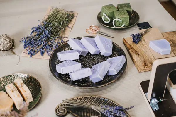Lavanta ve yeşil sabunlar kurumuş çiçeklerle ve kesme aletleriyle bir masaya dizilmiş. Aromaterapatik sabun, lavanta faydaları, fonksiyonel sağlık, bitkisel koku. Yüksek kalite fotoğraf
