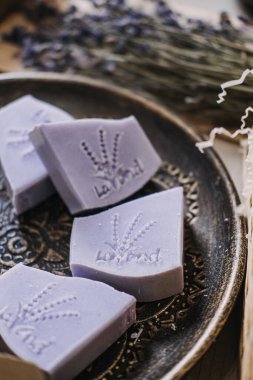 Botanik pullu lavanta sabunları kurumuş çiçeklerin yanındaki dekoratif bir tabakta duruyor. Doğal cilt bakımı, lavanta sabunu, botanik öz bakım, ekolojik bilinçli güzellik. Yüksek kalite fotoğraf