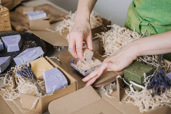 Kişi, el yapımı sabunlar ve kurutulmuş lavanta aksanlarıyla çevrili Kraft ambalajını damgalar. Ürün özelleştirme, eşsiz markalaşma tekniği, el yapımı cazibe, yaratıcı ürün kimliği. kalite fotoğraf