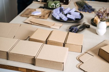 Temiz bir çalışma alanındaki el yapımı sabunların ve parçalanmış dolguların yanına yerleştirilmiş boş kraft kutuları. Ölçeklenebilir ambalaj, modüler kutu sistemi, ekommerce adaptasyon, kompakt ambalaj eğilimi. Yüksek kalite fotoğraf