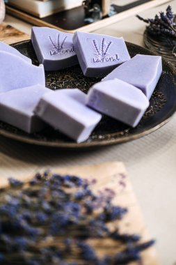 Kurumuş çiçeklerin yanında seramik bir tabakta sergilenen damgalı lavanta sabunları. Çevre dostu üretim, sürdürülebilir ürünler, sıfır atık sabun, el yapımı cilt bakımı. Yüksek kalite fotoğraf