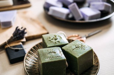 Yeşil damgalı sabunlar lavanta sabunları ve zanaatkar aletlerin yanında bir tabakta duruyor. Sanatsal süreç, bağımsız cilt bakımı, mikro marka kimlik, el yapımı güzellik ürünleri. Yüksek kalite fotoğraf