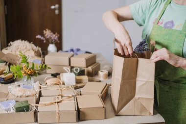 Kişi Kraft hediye çantaları ve el yapımı sabun kutularını doğal dekorlarla dolu bir çalışma masasına yerleştirir. Yaratıcı girişimci, esnaf ambalajı, marka özgünlüğü, yerel işletme. Yüksek kalite fotoğraf