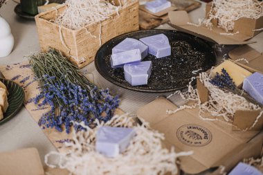 Kurumuş çiçeklerle sergilenen lavanta sabunları ve dinlendirici bir çalışma alanında kraft ambalajı. Lavanta sabunu, kişisel bakım trendleri, sakinleştirici ritüeller, sağlık yaşam tarzı. Yüksek kalite fotoğraf