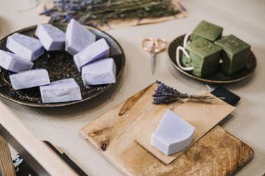 Lavanta ve yeşil sabunlar kurumuş çiçeklerle ve kesme aletleriyle bir masaya dizilmiş. Aromaterapatik sabun, lavanta faydaları, fonksiyonel sağlık, bitkisel koku. Yüksek kalite fotoğraf