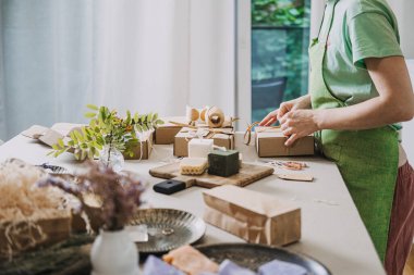 Kişi, doğal malzemeler ve el yapımı ürünlerle dolu parlak bir stüdyoda Kraft sabun kutularını hazırlıyor. Yavaş yapılan, dikkatli üretim, etik girişimcilik, amaç güdümlü iş. kalite fotoğraf