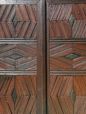 Simetrik geometrik desenleri ve tırnak detaylarını içeren kırsal ahşap bir kapının yakın çekimi. Geleneksel işçilik, mimari yapı, ahşap işçiliği, kültür mirası. Yüksek kalite