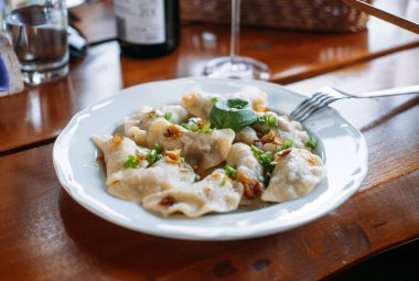 Üzerinde karamelli soğan ve otlarla kaplı bir tabak pierogi, arka planda şarap ve ahşap bir masada servis edilir. Yerel kaynaklar, taze tarım gıdaları, sürdürülebilir yemekler, kırsal kesimler.