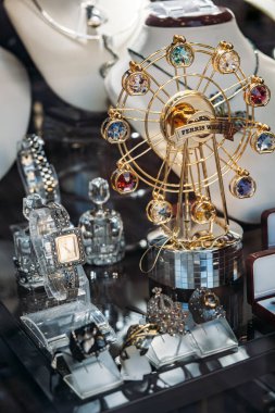 Süslü yüzükler, lüks saatler ve dönme dolap temalı mücevher sergisi olan bir kuyumcu dükkanının penceresinin yakın çekimi. Lüks aksesuarlar, görsel pazarlama, hediye ekonomisi, perakende hikaye anlatımı. Yüksek