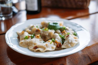 Ahşap bir masada servis edilen kızarmış soğan ve otlarla süslenmiş geleneksel pierogi tabağı. Leh pierogi, miras tarifleri, aşçılık özgünlüğü, geleneksel hamur tatlısı. Yüksek kalite fotoğraf