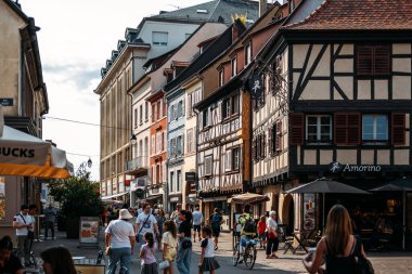 Colmar 'da renkli cepheli, yarı keresteli evler, dükkanlar, kafeler ve güneşli bir yaz gününde yürüyen insanlar ile dolu bir cadde, Fransa' nın Alsace bölgesi, 20 Ağustos 2025. Yüksek kalite fotoğraf