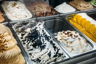 Çerez, krema, şam fıstığı ve karamel karışımı da dahil olmak üzere metal bir vitrinde birden fazla dondurma aroması var. Sanatsal tatlılar, lezzet çeşitliliği, hoşgörülü ikramlar, yerel gelateria kültürü. Yüksek kalite