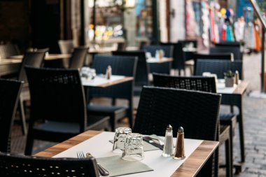 Çağdaş kafe terasında kaldırım taşı bir sokakta düzgün düzenlenmiş masalar ve sandalyeler. Şehir sakinliği, sessiz lüks, yumuşak minimalizm, rafine yemek. Yüksek kalite fotoğraf