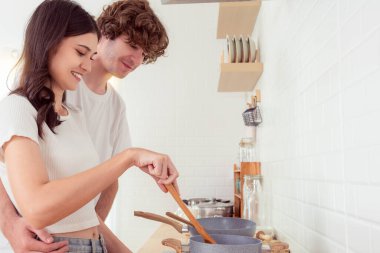 Sevimli genç bir çift mutfakta birlikte yemek pişiriyor gülümsüyor güzel bir kadın yemek pişiriyor ve yakışıklı bir adam karısına bakıyor yemek pişiriyor ve birlikte mutfakta vakit geçiriyorlar güzel sevgili ve sevgili 