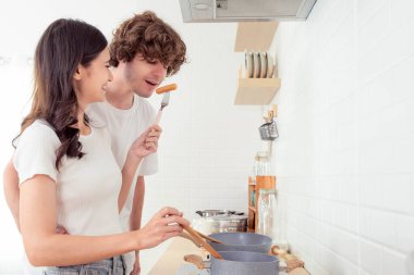 Aşk çifti sabah kahvaltısı için mutfakta yemek pişiriyor. Sevgilisi, Mutluluk 'u yediği için erkek arkadaşına sosis veriyor. Gülümseyen çift evde birlikte yemek pişiriyor. 