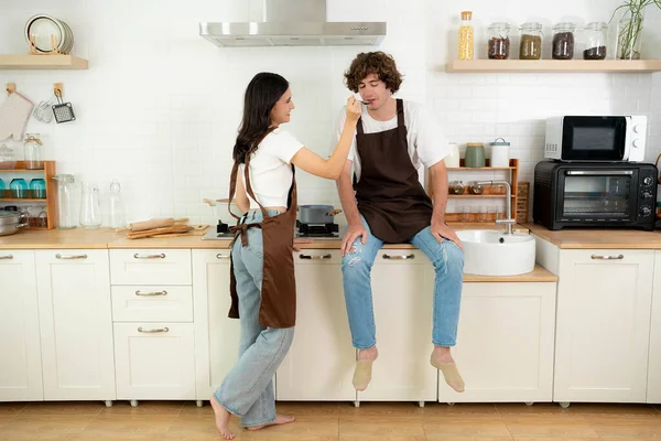 Couple cooking in kitchen Man taste food from girlfriend Happy couple at home enjoying life together relationship Girl giving food to Man to taste Wife cooking for her husband Male and female enjoying