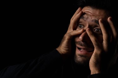 Korkmuş genç sakallı adam, korku ifadesi yüzünden korkmuş ve dehşete düşmüş. Yüzüne dokunmuş. Genç adam, korku odası duygusal ve yüz ifadesi konseptinde şok ve panik halindeydi.