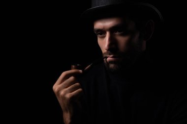 Dedektif ya da casus adam pipo içiyor yakışıklı genç sakallı adam pipo içiyor kafasını çeviriyor ve karanlık oda modası ve modaya uygun bir şeyler planlıyor.