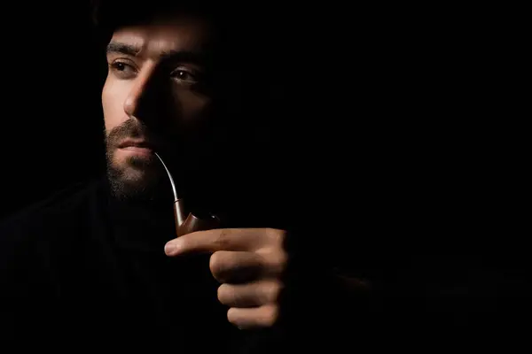 Detective or Spy man smoking pipe Portrait handsome young bearded guy wear top hat smoking a pipe He looking away and thinking planning something in the dark room retro style and retro fashion concept