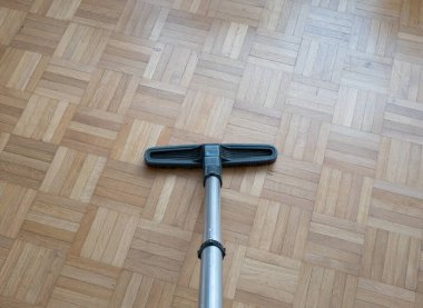 Household vacuum cleaner brush and extension rod on laminated wooden tile surface inside a generic apartment. Close up downwards looking shot, no people.