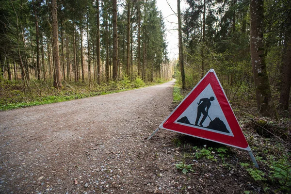 Road works or men at works tringle sign on the side of a forest road in Europe. Trees in the background, no people, dirt road.
