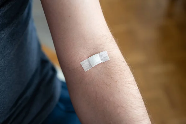 Small plaster or bandaid on the arm of an unrecognizable Caucasian male. Plastered on the elbow pit to stop bleeding after blood collection.