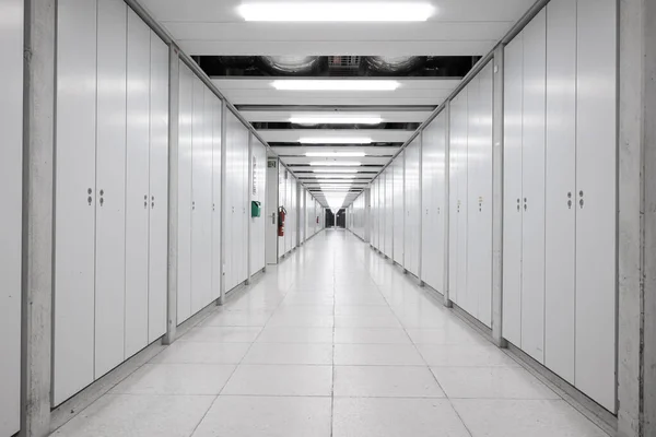 stock image Long interior empty corridor hallway illuminated by neon lights with locker doors across both side, no people.