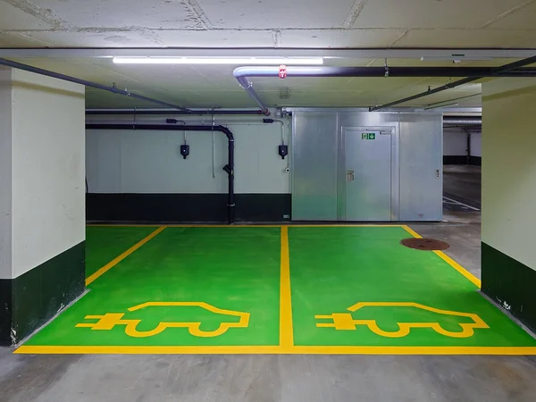 Underground parking spaces reserved for electric vehicles only. Small wall mounted charging plugs, green painted cement floor, no people.