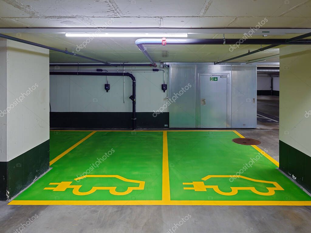 Underground parking spaces reserved for electric vehicles only. Small wall mounted charging plugs, green painted cement floor, no people.