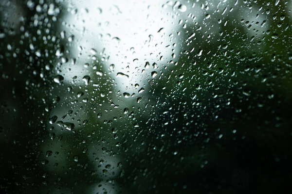 Rain water droplets accumulating on a car's window glass. Close up shot, shallow depth of field, no people, selective focus.