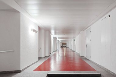 Uzun, boş bir koridor ya da koridor. Duvara ve tavana ışık monte edildi, insan yok.