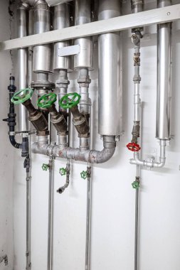 Endüstriyel boyutta duvar monte edilmiş su boruları. Büyük boş oda, insan yok.