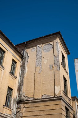 Harap olmuş bina cephesi. Çatlamış ve soyulmuş dış alçı tuğla duvar ve eski pencere çerçeveleri, insan yok..