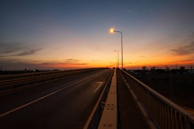 Alacakaranlıkta beton köprü silueti. Parlayan sokak lambası, geniş açı, insan yok.