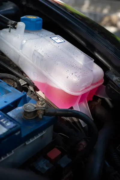 Car coolant liquid or antifreeze expansion tank or bottle, mounted in an engine bay. Close up shot, no people, pink G12 coolant inside.