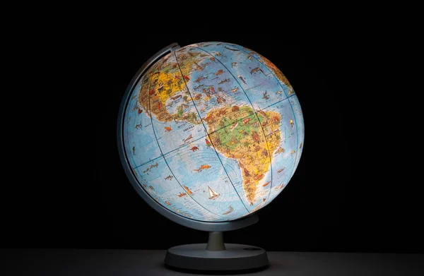 Illuminated earth globe in the form of a desk or table night light, glowing in the dark, no people.