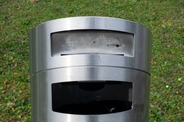 Paslanmaz metal çöp tenekesi ve sigara küllüğü. Yakın çekim, yeşil arkaplan, insan yok..