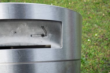 Paslanmaz metal çöp tenekesi ve sigara küllüğü. Yakın çekim, yeşil arkaplan, insan yok..