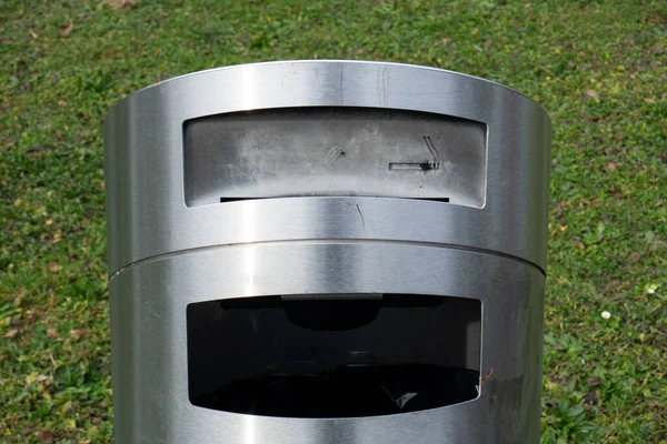 Paslanmaz metal çöp tenekesi ve sigara küllüğü. Yakın çekim, yeşil arkaplan, insan yok..