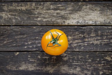 Kaba ahşap bir zeminde izole edilmiş tek olgun sarı domates. Yakın çekim, insan yok.