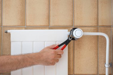 Ev radyatörünün termostatını tamir eden iğneli penseyle beyaz bir erkek eli. Yakın çekim, yüzü yok, tanınmayan bir adam..