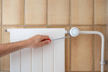 Beyaz erkek eli elinde tornavidayla kaloriferin termostatını tamir ediyor. Yakın çekim, yüzü yok, tanınmayan bir adam..