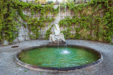 Kadın bronz heykeli ve Avrupa 'da bir kasabada eski bir taş parkı çeşmesi ve fıskiye. Güneşli yaz günü, kimse yok..