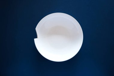 Kırık ya da kırık beyaz seramik çorba tabağı koyu mavi arka planda, üst manzara, insan yok.