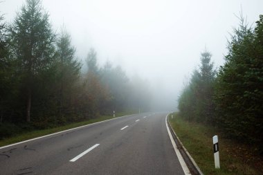 Tick autumn morning fog covered empty rural road through a forest in Europe. Wide angle view, limited visibility, bad driving weather concept, no people. clipart