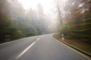 Long exposure, blurry autumn morning covered empty rural road through a forest in Europe. Wide angle view, limited visibility, bad driving weather concept, no people clipart