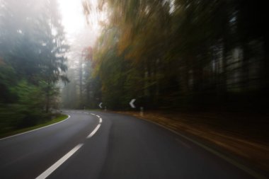 Long exposure, blurry autumn morning covered empty rural road through a forest in Europe. Wide angle view, limited visibility, bad driving weather concept, no people clipart