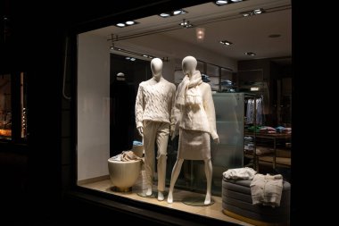 Female mannequins in store glass window display dressed casual autumn winter elegant clothing, night scene. clipart